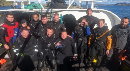 12 divers pose on the dive deck in their drysuits