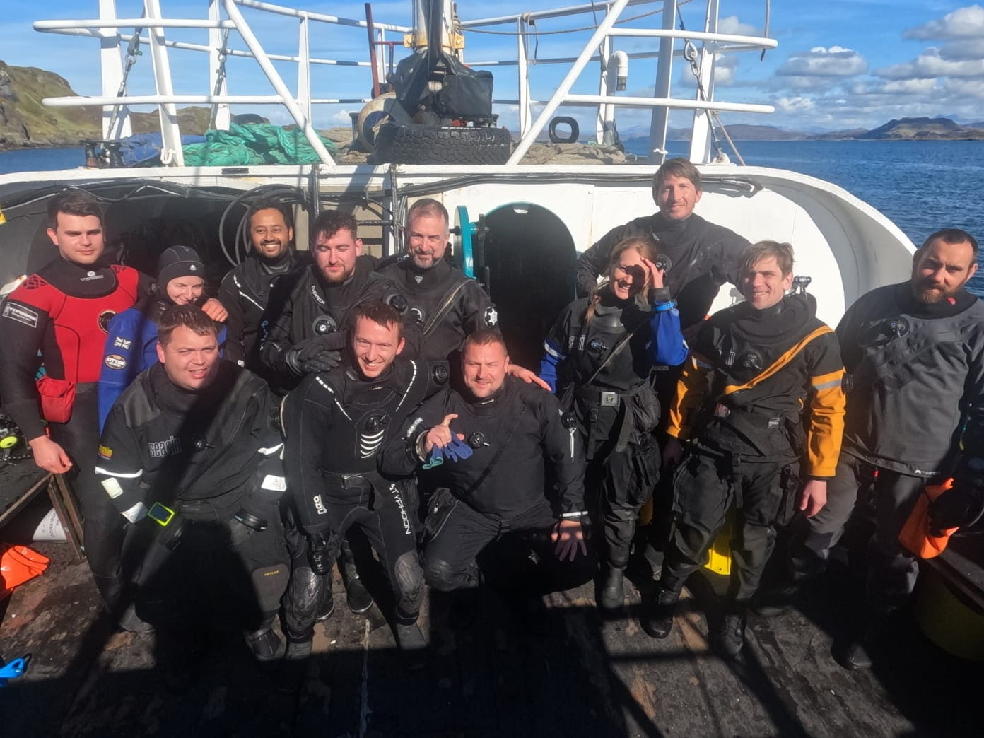 12 divers pose on the dive deck in their drysuits